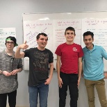 Four young men in front of slip chart paper. One with a thumb up.