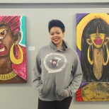 An employee standing in front of her artwork during a company art show displayed in the office