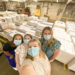 The KC interns taking a selfie in front of the paper waiting to be made into books.