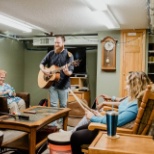 person playing guitar for two people sitting in chairs